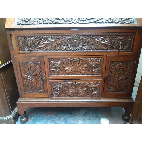 1117 - A JACOBEAN REVIVAL HEAVILY CARVED OAK BUREAU WITH TWO LOWER DOORS, TWO SHORT DRAWERS AND ONE LONG DR... 