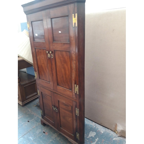 1125A - A GEORGIAN FLAMED MAHOGANY CORNER CUPBOARD WITH TWO LONG UPPER AND TWO SHORT LOWER DOORS WITH BRASS ... 