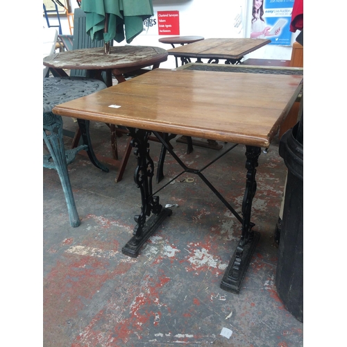 22 - A SQUARE TOPPED WOODEN PATIO TABLE ON HEAVY ORNATE CAST IRON BASE