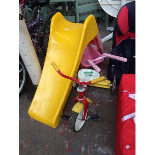 23 - THREE CHILD'S OUTDOOR TOYS TO INCLUDE A PINK AND YELLOW PLASTIC SLIDE, A RED AND YELLOW RALEIGH TRIC... 