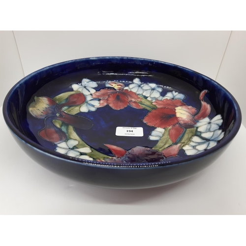 194 - A LARGE ENGLISH WILLIAM MOORCROFT POTTERY BOWL IN THE ORCHID PATTERN ON A DARK COBALT BLUE GROUND WI... 