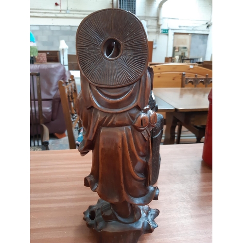 110 - A 19TH CENTURY ORIENTAL CARVED HARDWOOD FIGURE OF AN ELDER HOLDING FOOD BASKET