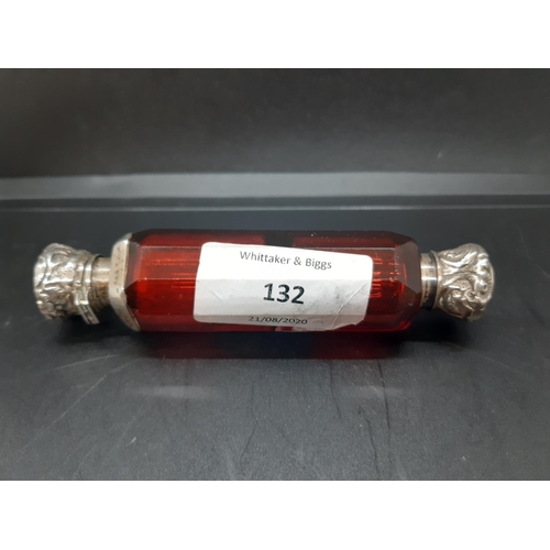 132 - A double ended ruby glass scent bottle with embossed white metal tops with repeated foliate design, ... 