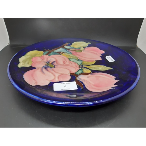 6 - A Moorcroft pottery plate in the pink magnolia pattern on blue ground - measuring approx. 25cm in di... 