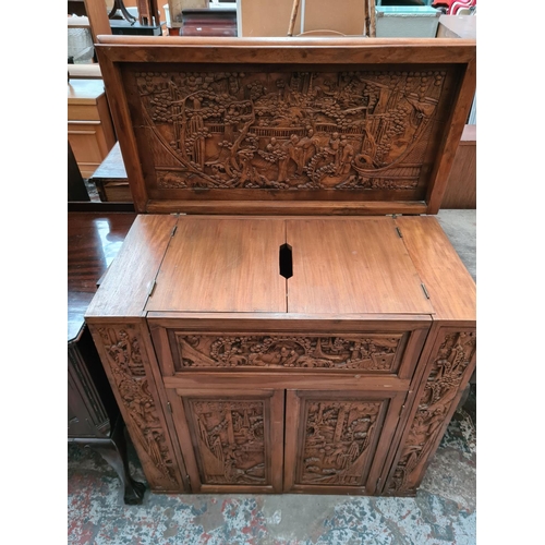 504 - An oriental carved teak concealed cocktail cabinet with hinged lid, eight place bottle holder, two l... 