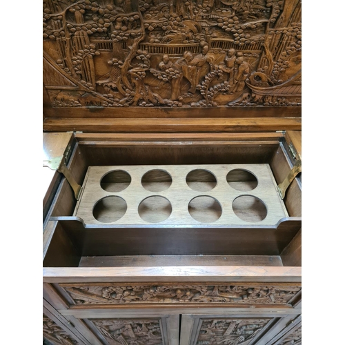 504 - An oriental carved teak concealed cocktail cabinet with hinged lid, eight place bottle holder, two l... 