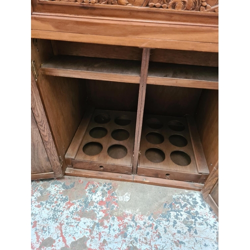 504 - An oriental carved teak concealed cocktail cabinet with hinged lid, eight place bottle holder, two l... 