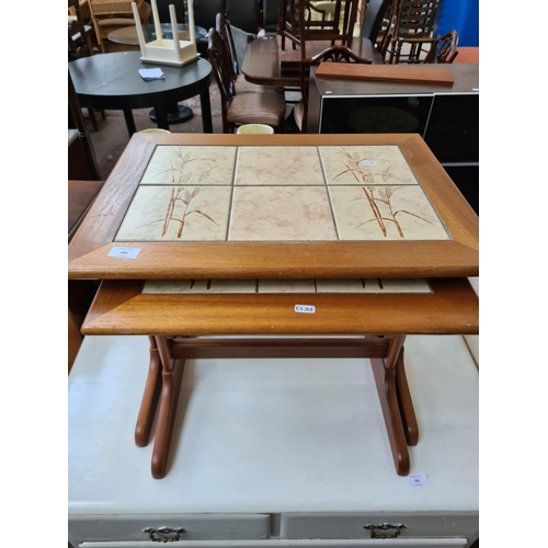 586 - A teak nest of two tables with tile inserts