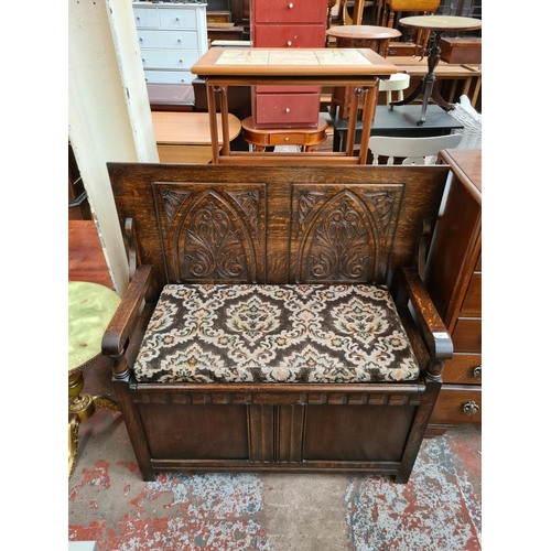 608 - An Arts and Crafts style oak monks bench with carved back and hinged seat - measuring approx. 103cm ... 