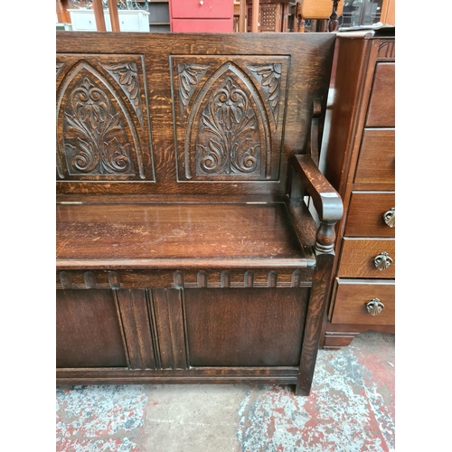 608 - An Arts and Crafts style oak monks bench with carved back and hinged seat - measuring approx. 103cm ... 