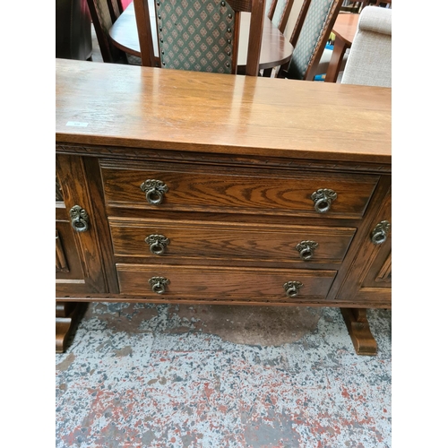 628 - An Old Charm oak sideboard with two outer cupboard doors and three central drawers - measuring appro... 