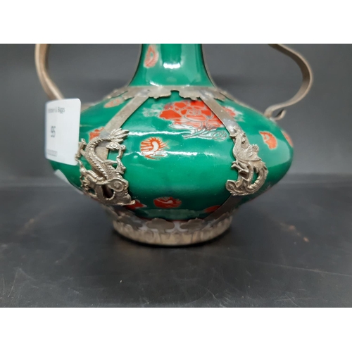 95 - An oriental ceramic and white metal ewer on hand painted green ground with rose detailing and dragon... 