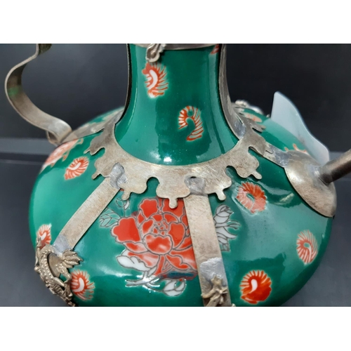 95 - An oriental ceramic and white metal ewer on hand painted green ground with rose detailing and dragon... 