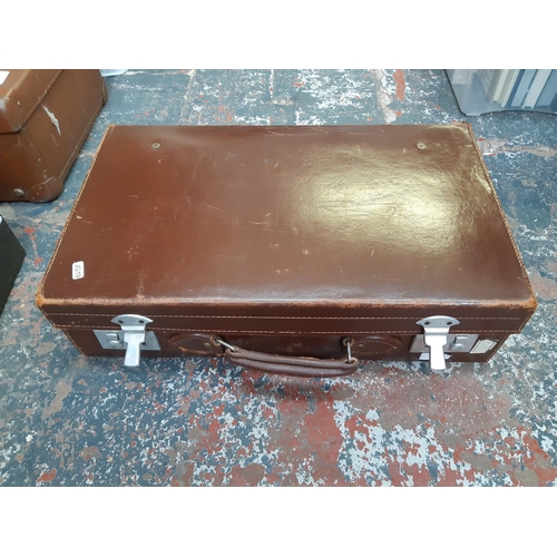 335 - A vintage brown cow hide leather suitcase with various travel stickers and chrome plated locks