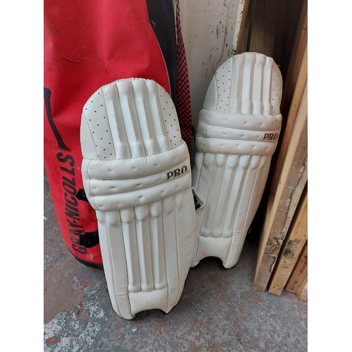 766 - A large black and red Gray Nicolls cricket bag containing Gunn & Moore cricket bat, wickets, batting... 