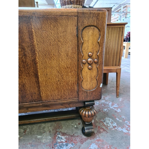 551 - An Art Deco oak sideboard on heavily carved baluster supports with two central cupboard doors, one o... 