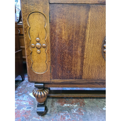 551 - An Art Deco oak sideboard on heavily carved baluster supports with two central cupboard doors, one o... 