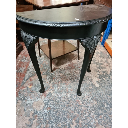 557 - Two items to include an Edwardian oak two tier side table and a modern black painted half moon conso... 