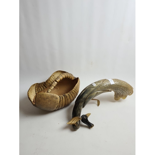 183 - Two items, a taxidermy armadillo shell basket and a carved horn peacock bird figurine (A/F)