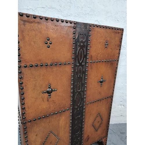 424 - An Arts and Crafts brass studded leather two section stick stand with carved oak centre panel and ma... 