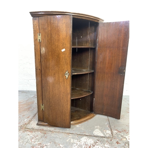 708 - A Georgian oak bow front wall mountable corner cabinet with brass 'H' hinges and three internal shel... 