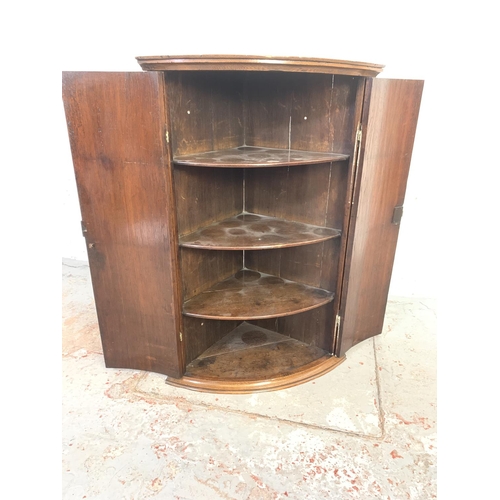 708 - A Georgian oak bow front wall mountable corner cabinet with brass 'H' hinges and three internal shel... 