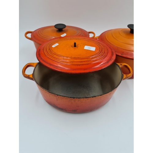 507 - Three orange enamel and cast iron lidded casserole dishes, two being Le Creuset