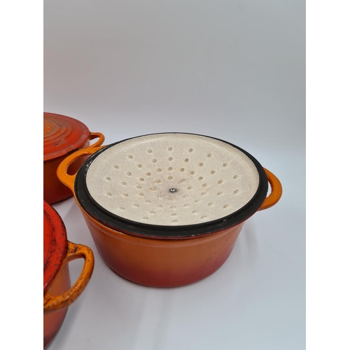 507 - Three orange enamel and cast iron lidded casserole dishes, two being Le Creuset