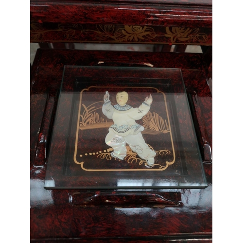 110 - An Oriental red lacquered nest of four tables with hand painted and mother of pearl Geisha girl desi... 