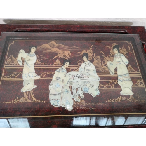 110 - An Oriental red lacquered nest of four tables with hand painted and mother of pearl Geisha girl desi... 