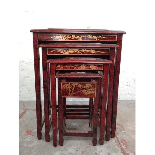 110 - An Oriental red lacquered nest of four tables with hand painted and mother of pearl Geisha girl desi... 