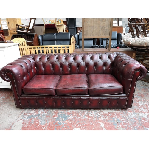 67 - An oxblood leather Chesterfield three seater sofa - approx. 72cm high x 195cm wide x 85cm deep