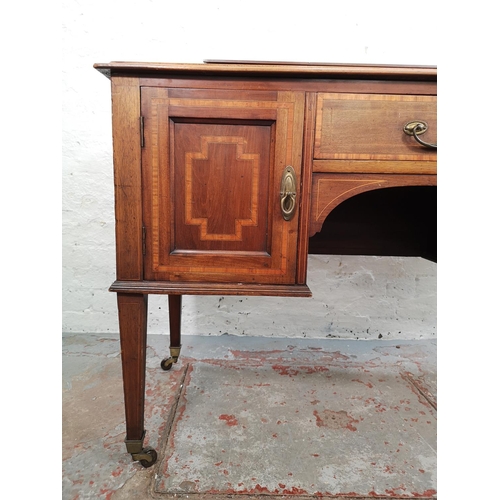 73 - An Edwardian inlaid mahogany desk with central drawer, two outer cupboard doors and tapering support... 