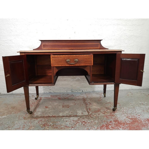 73 - An Edwardian inlaid mahogany desk with central drawer, two outer cupboard doors and tapering support... 