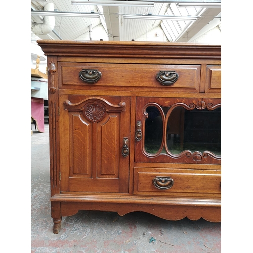 75 - An Art Nouveau oak sideboard with two upper drawers, two outer cupboard doors, central glazed door w... 