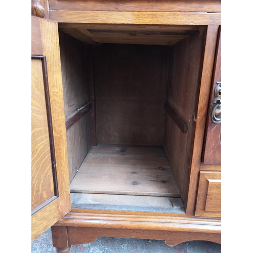 75 - An Art Nouveau oak sideboard with two upper drawers, two outer cupboard doors, central glazed door w... 