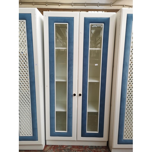 1060 - A contemporary white painted and blue fabric bedroom display cabinet with two bevelled glass doors a... 