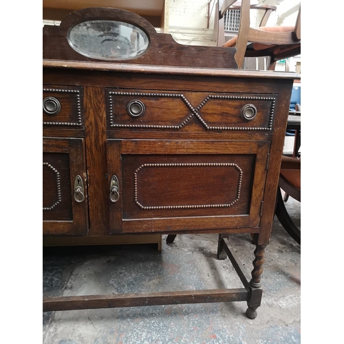 1082 - A 1920s oak mirror back sideboard with two drawers, two cupboard doors, oval bevel edged mirror and ... 