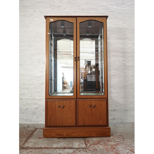 1055B - A late 20th century teak effect display cabinet with two upper bevelled glass doors, two lower cupbo... 