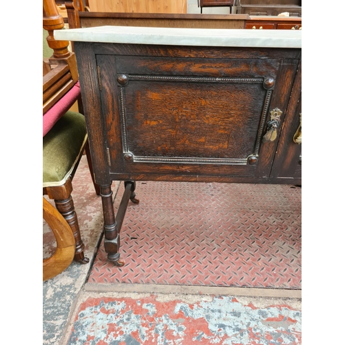 88 - An early 20th century oak and marble top two door wash stand - approx. 75cm high x 108cm wide x 48cm... 