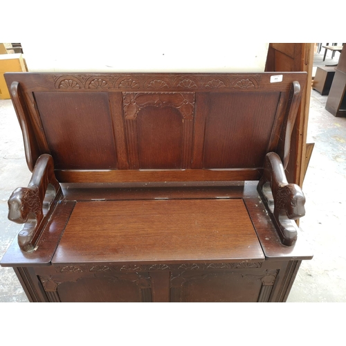 253 - A mid 20th century oak monks bench with lion design armrests and hinged lid - approx. 98cm high x 95... 