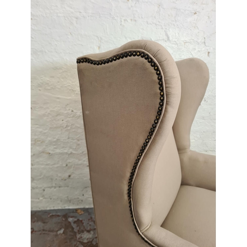 412 - An early 20th century beige upholstered wingback armchair with mahogany supports and casters - appro... 