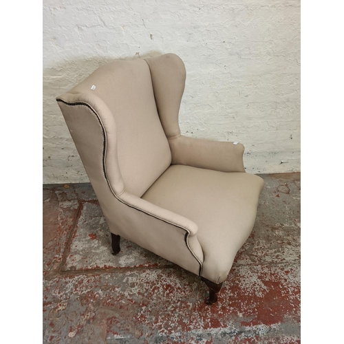 412 - An early 20th century beige upholstered wingback armchair with mahogany supports and casters - appro... 