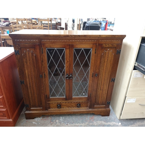 393 - An oak linenfold bookcase with two outer cupboard doors, two central leaded glass doors and single l... 