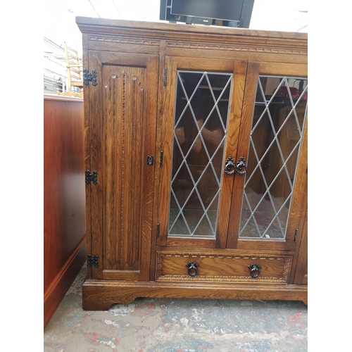 393 - An oak linenfold bookcase with two outer cupboard doors, two central leaded glass doors and single l... 