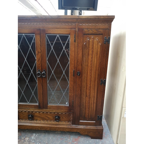 393 - An oak linenfold bookcase with two outer cupboard doors, two central leaded glass doors and single l... 