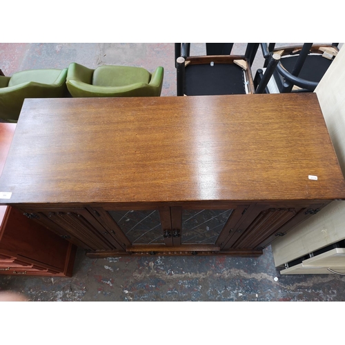 393 - An oak linenfold bookcase with two outer cupboard doors, two central leaded glass doors and single l... 