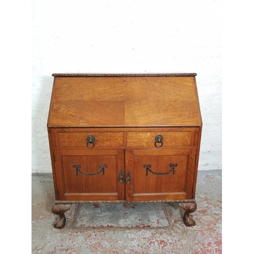 401 - An early/mid 20th century oak bureau with two drawers, two cupboard doors, fall front, ball and claw... 