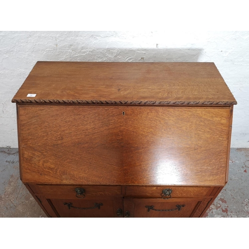 401 - An early/mid 20th century oak bureau with two drawers, two cupboard doors, fall front, ball and claw... 