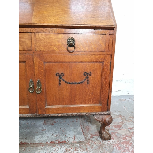 401 - An early/mid 20th century oak bureau with two drawers, two cupboard doors, fall front, ball and claw... 